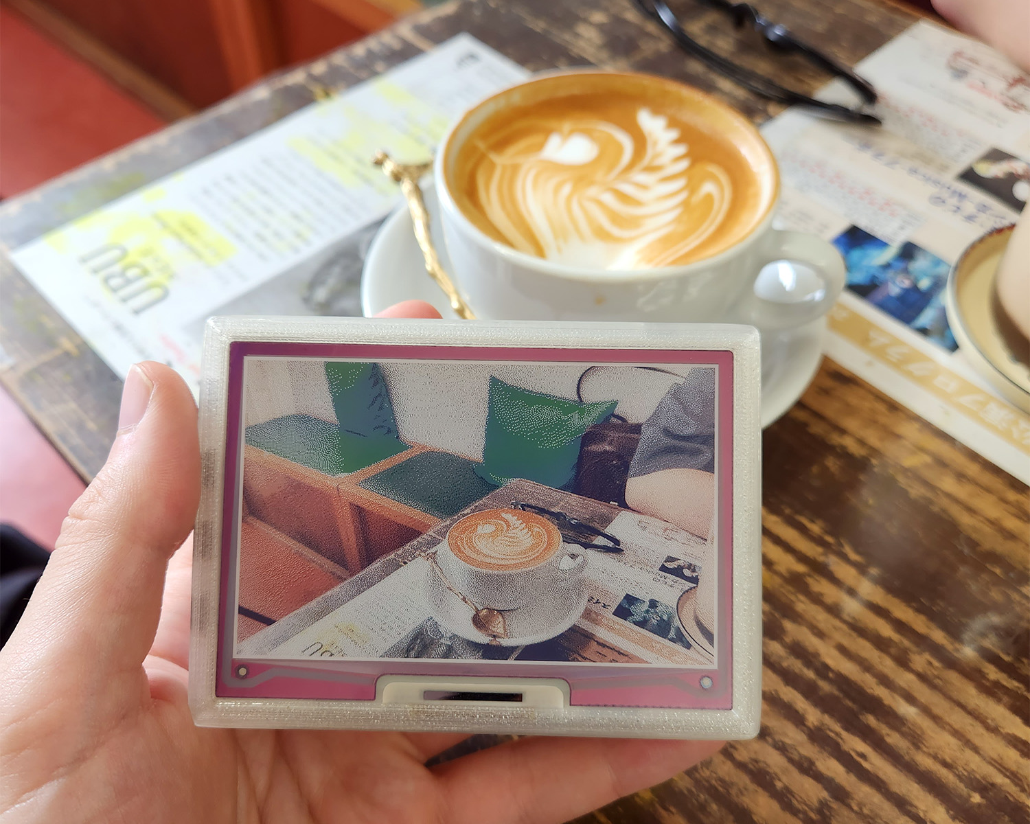 Photo of a hand holding eink.cam with a photo of a coffee cup