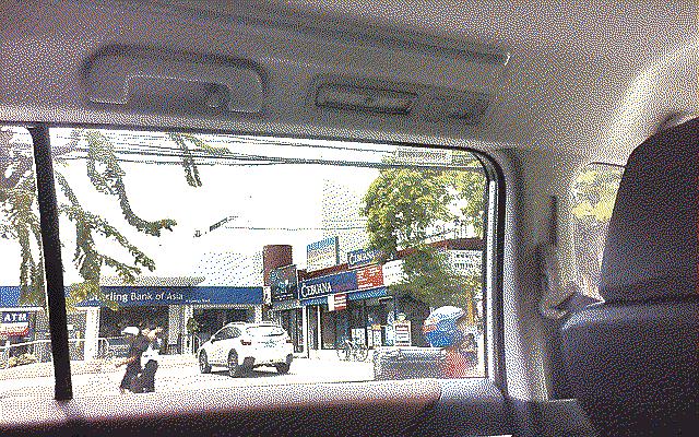 A corner with a bank and shops, shot through a car window