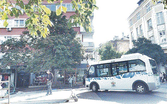 A small electric bus and a worker cleaning the street