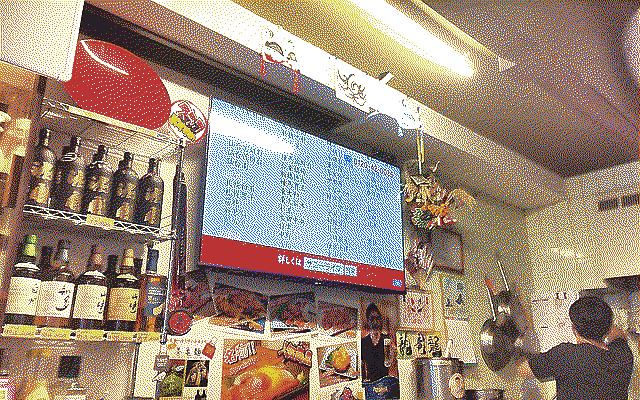 Inside the restaurants, there’s bottles of liquor on the wall and a big TV. The owner can be seen on the right cooking.